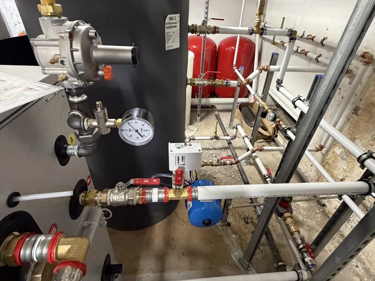 Les raccordements hydrauliques et gaz du ballon d’eau chaude sanitaire : vannes, manomètre, vase d’expansion bleu et tuyauterie multicouche sur rails.