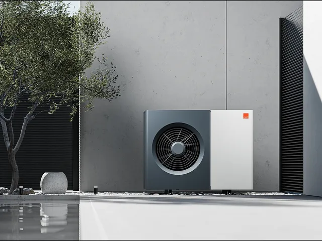 Une pompe à chaleur air/eau extérieure posée devant le mur en béton d’un bâtiment contemporain, à côté d’un olivier et d’un bassin.